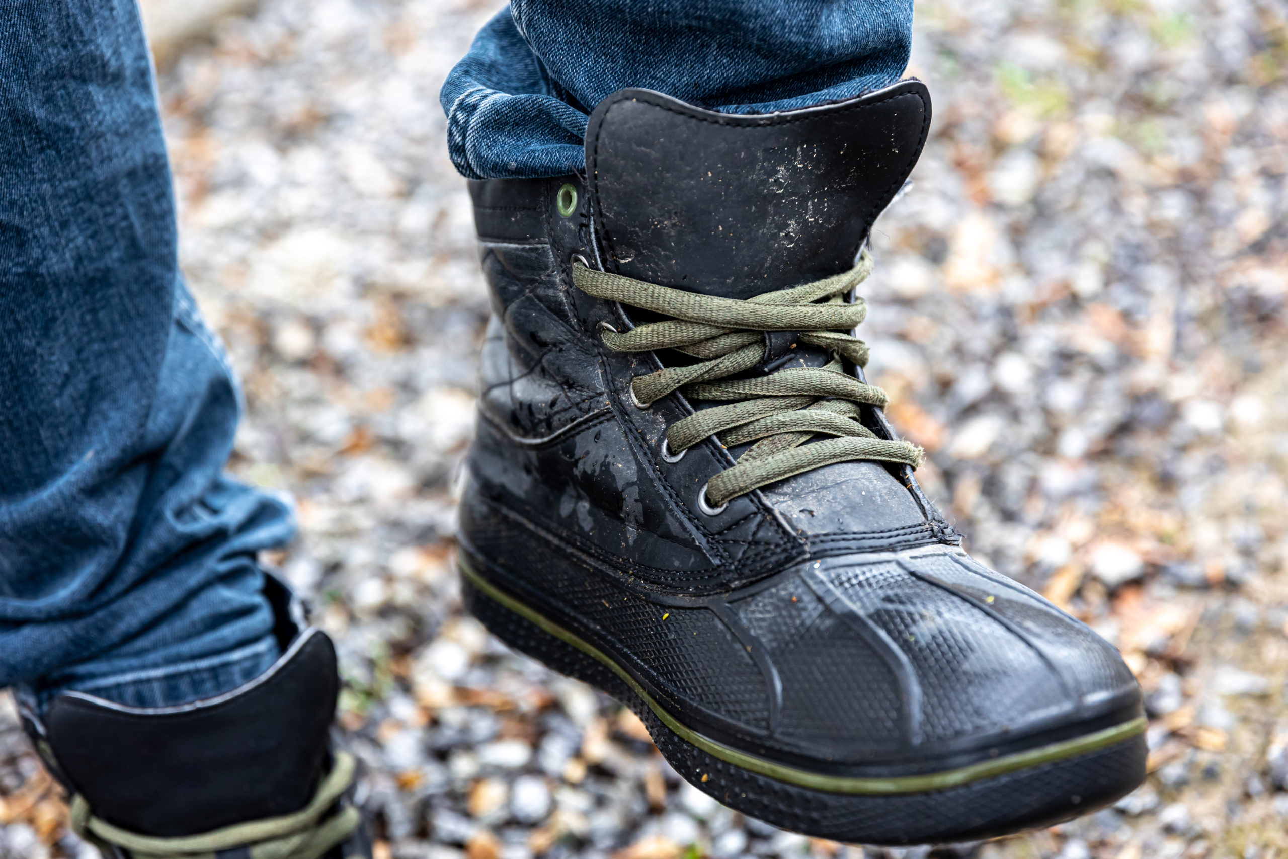 A man in boots stands on gravel, close up.